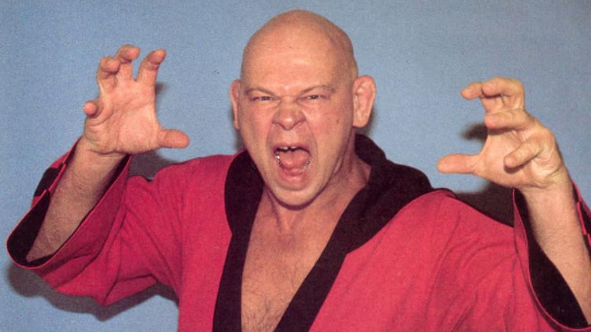 Baron von Raschke wearing a red gown with his hands raised and snarling, posing in a studio