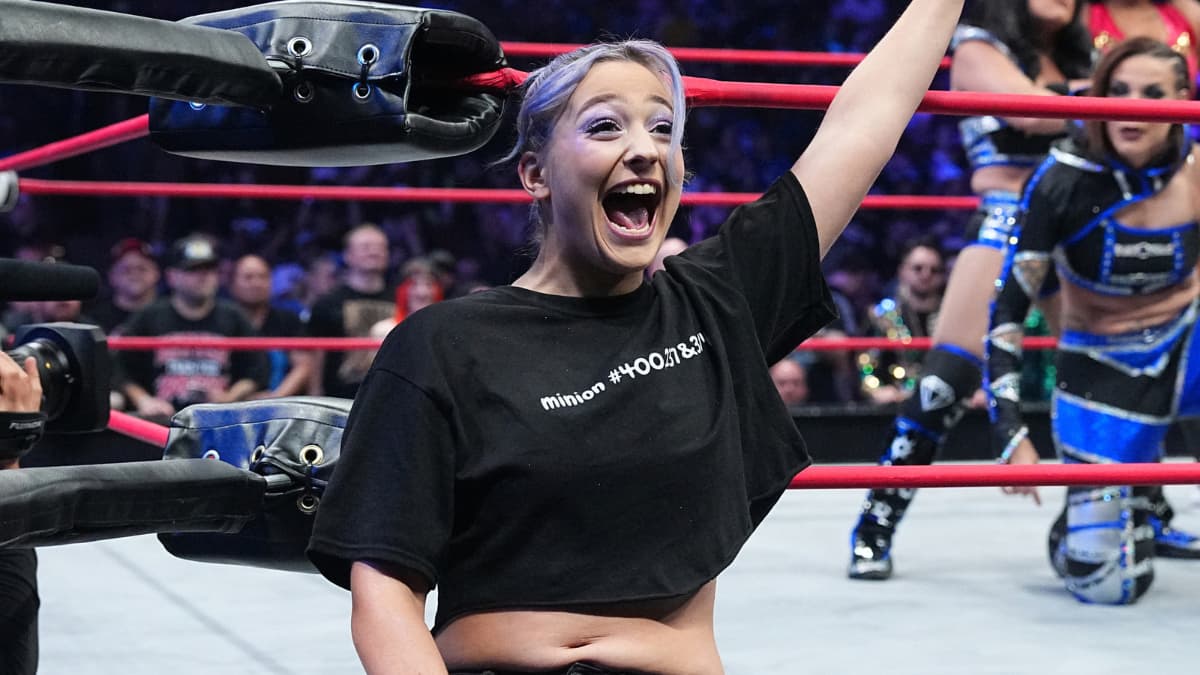 Billie Starkz outside a wrestling ring happily yelling and waving at the audience