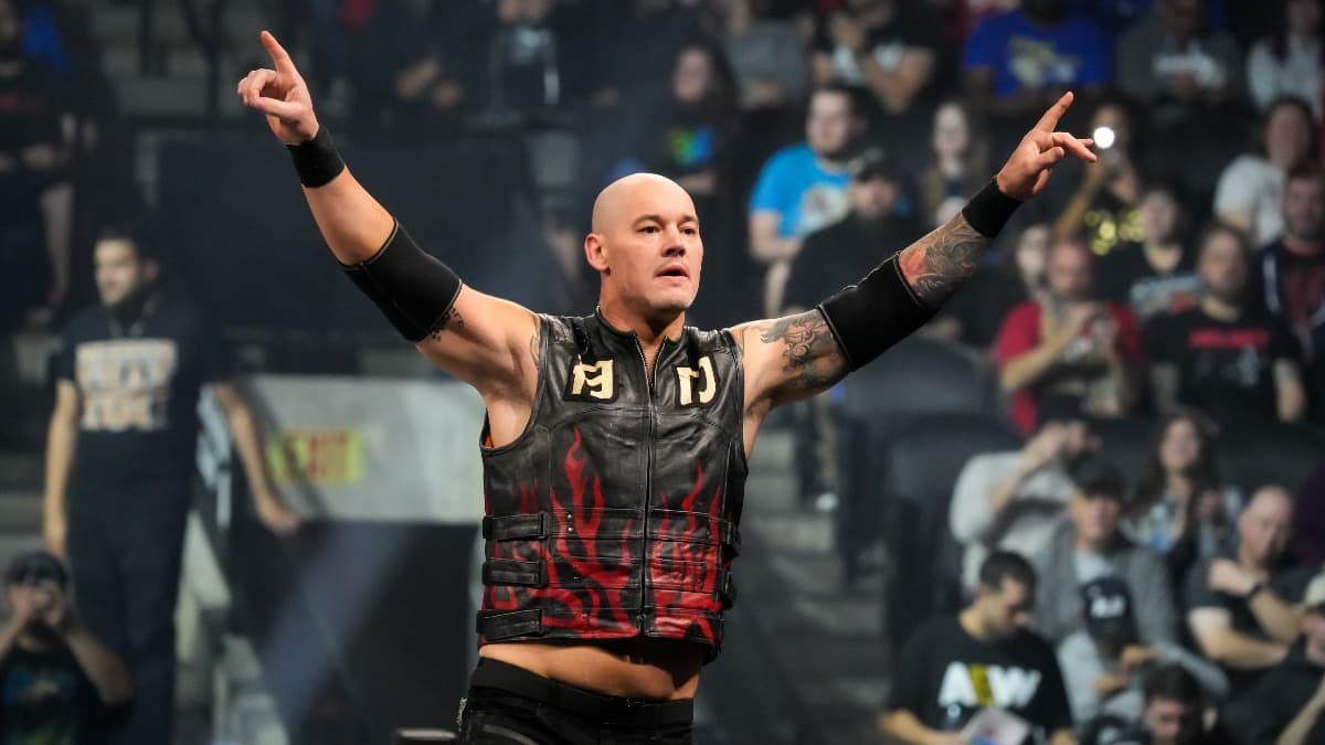 Bishop Dyer wearing a black leather vest with flames on with his arms outstretched while standing on pro wrestling turnbuckle