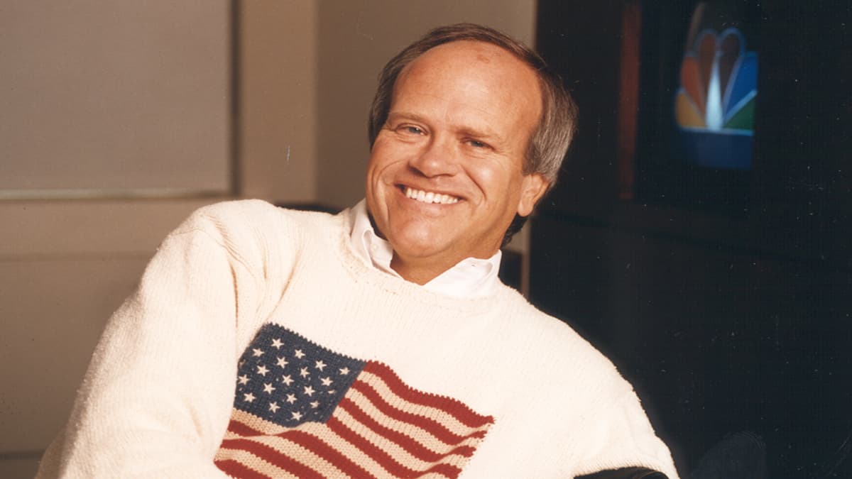 Dick Ebersol in a US flag jumper lounging in a chair and smiling