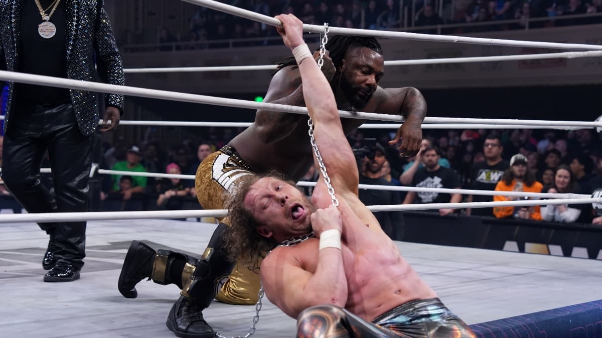 Swerve Strickland smirking while holding a chain that is storyline choking Kenny Omega