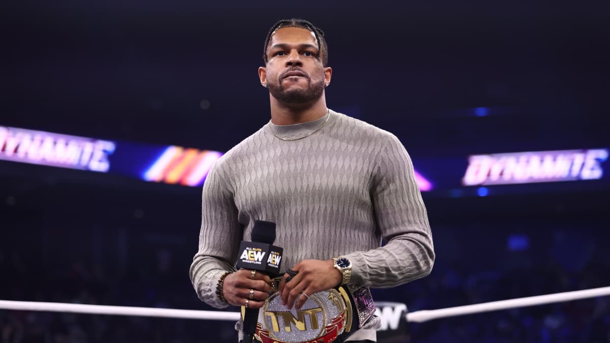Kevin Knight wearing a grey sweater with the TNT Title around his waist looking angry