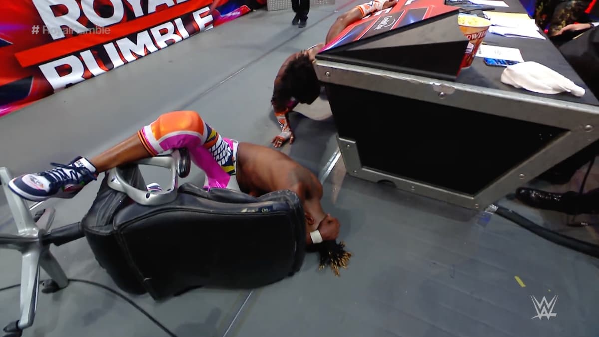Kofi Kingston crumpled on the floor with his foot on a computer chair