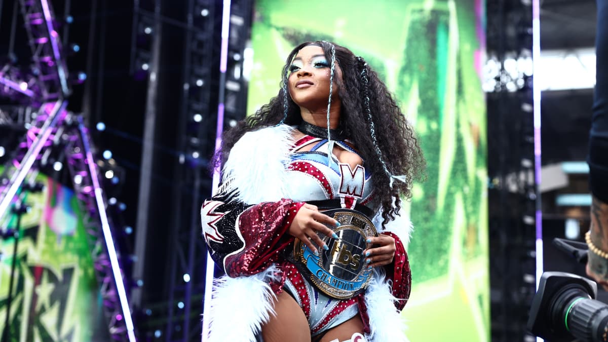 Maya World wearing a big white coat and wearing the TBS Title
