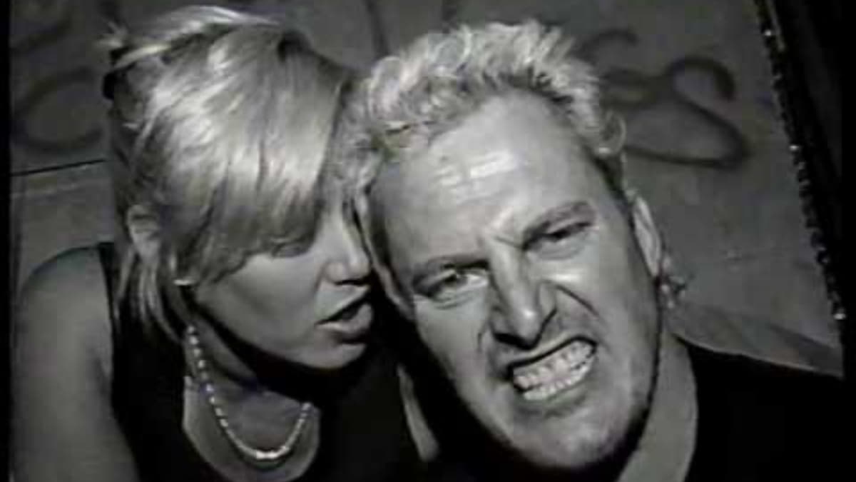 Sandman baring his teeth as Missy Hyatt whispers into his ear