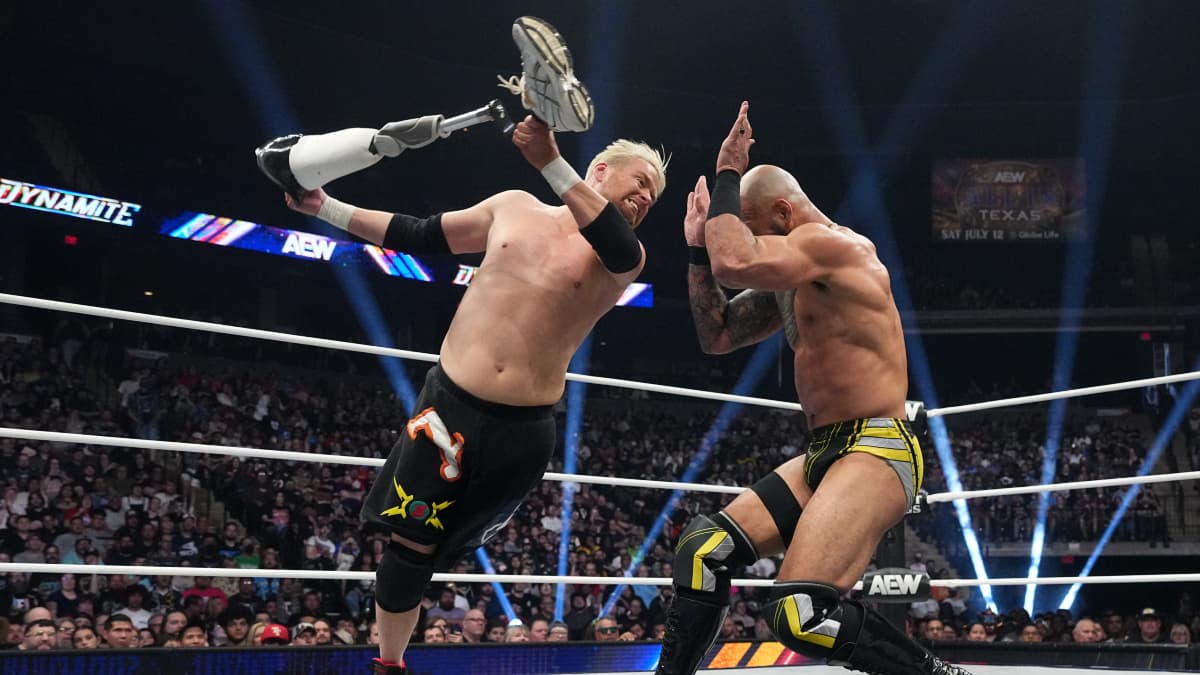 Zach Gowen holding his own leg about to hit Ricochet on the head with it