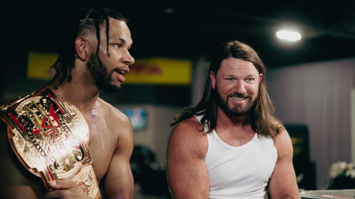 AJ Styles in a white vest looking giddy alongside a sweaty Leon Slater on the left