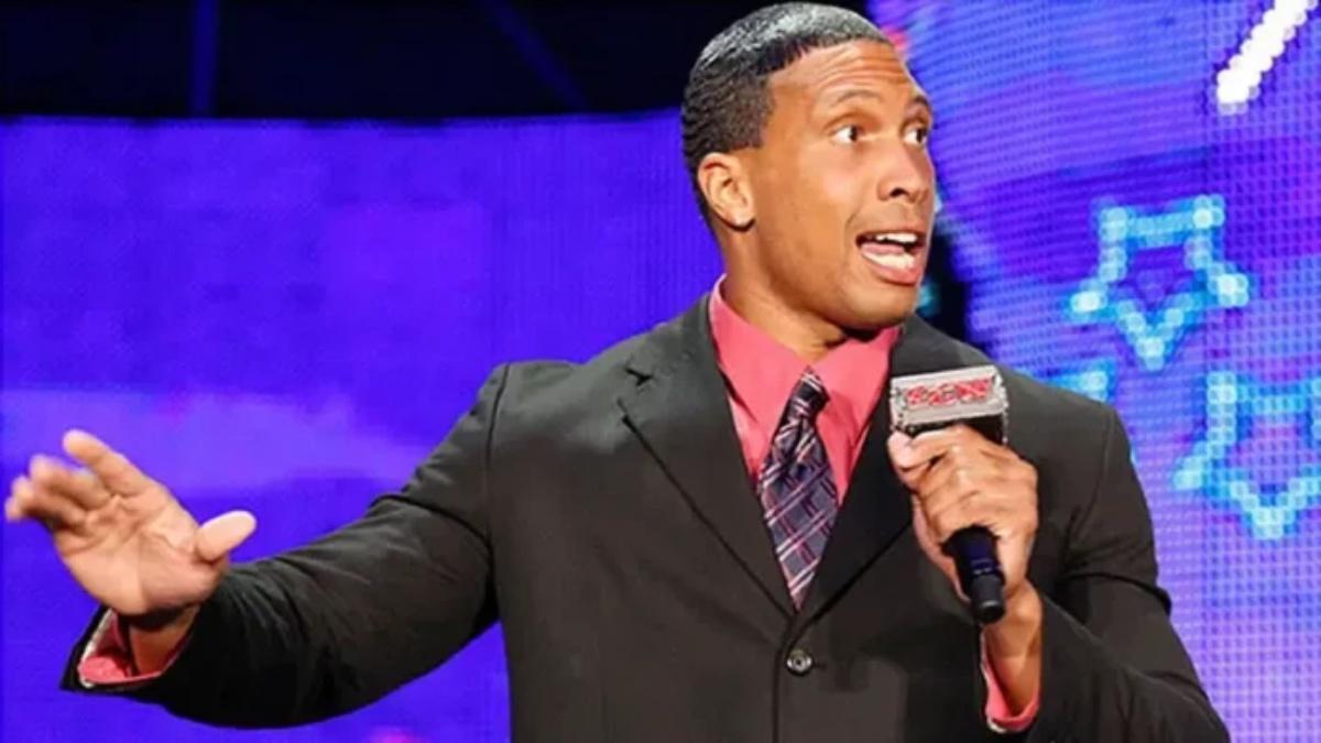 Abraham Washington in a black suit with a pink shirt and holding an ECW microphone