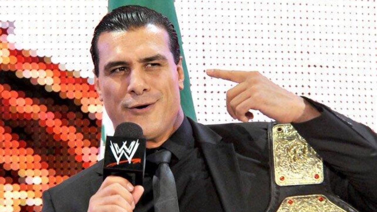Alberto Del Rio pointing to his ear while wearing a black suit