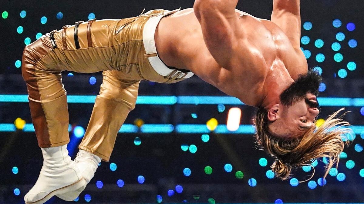 Andrade mid-moonsault wearing Gold/Brown trousers