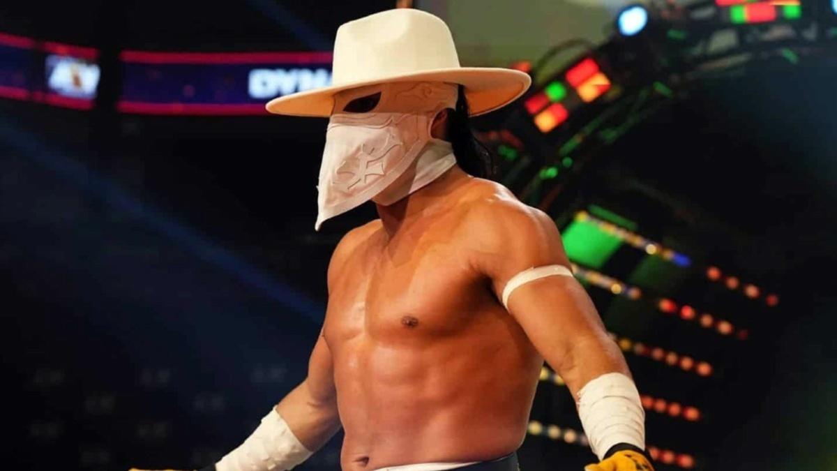 Bandido in a white hat walking to the ring with blurred lights in the background.