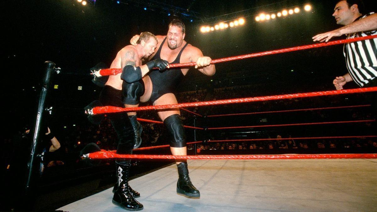 The Big Show kneeing Diamond Dallas Page in the corner of a pro wrestling ring