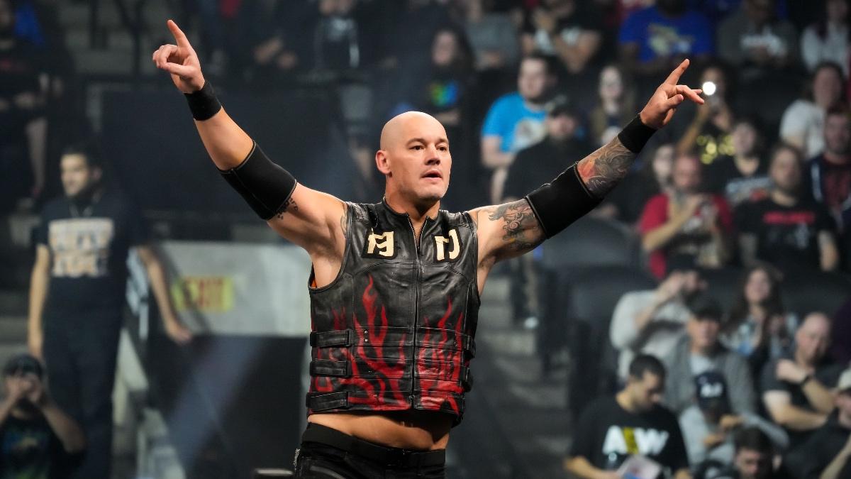 Bishop Dyer wearing a black leather vest with flames on with his arms outstretched while standing on pro wrestling turnbuckle