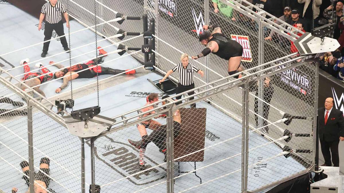 Bronson Reed diving off the top of the WarGames cage as CM Punk helps Roman Reigns off a table below