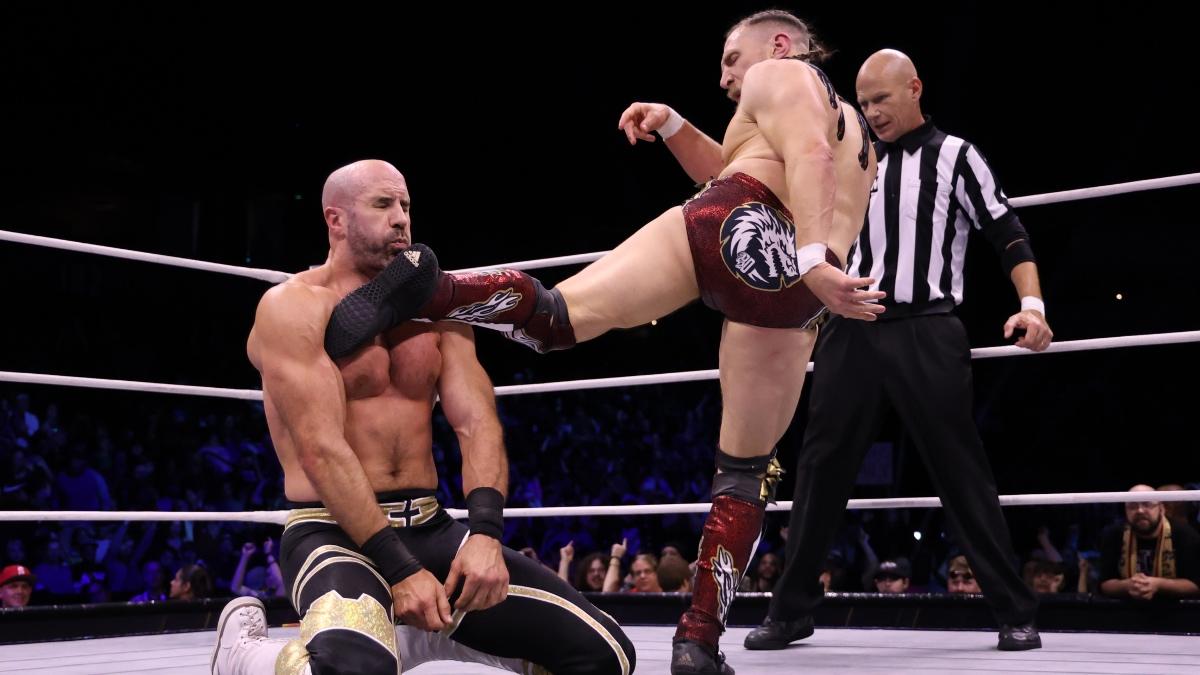 Bryan Danielson in red trunks kicking Claudio Castagnoli in black pants 