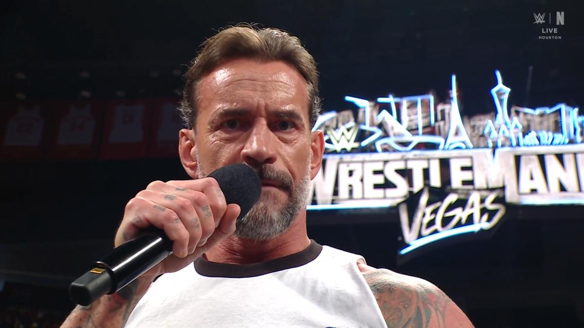 CM Punk holding a microphone to his lips as the WrestleMania 42 banner is in the background