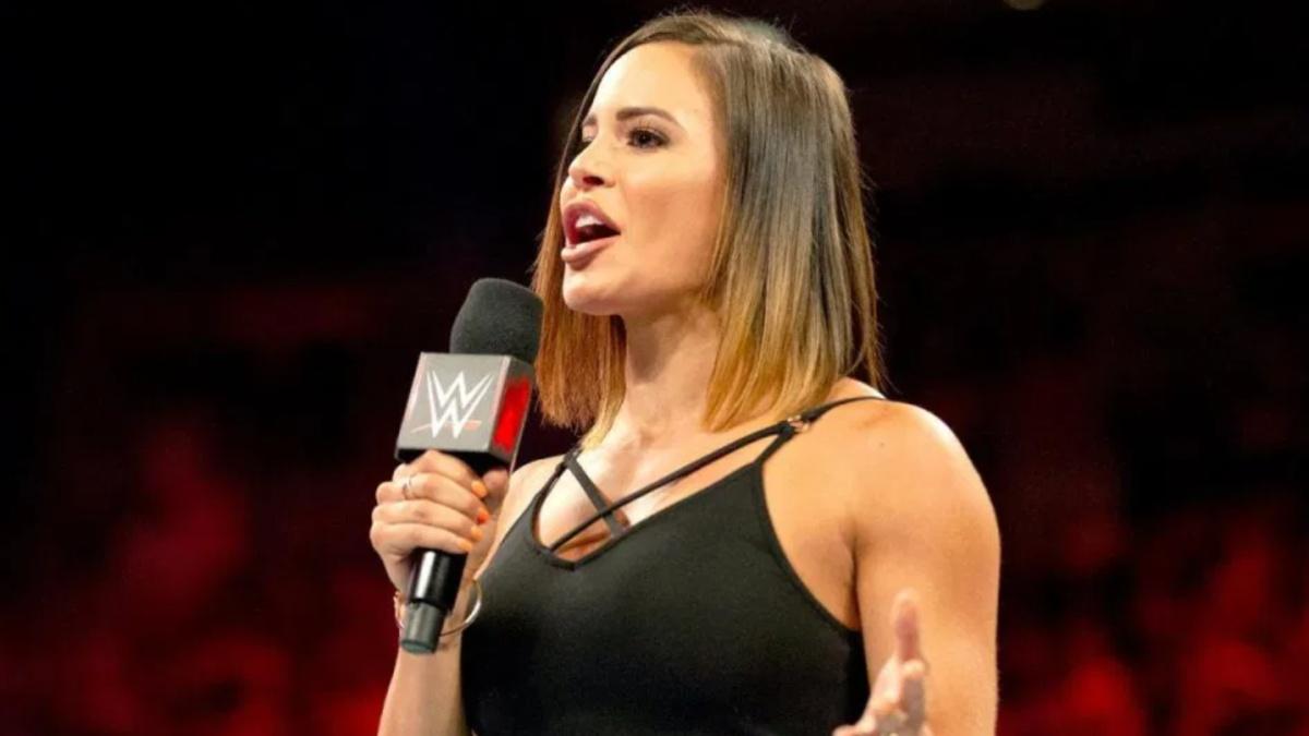 Charly Caruso in a black top holding a WWE microphone in a wrestling ring