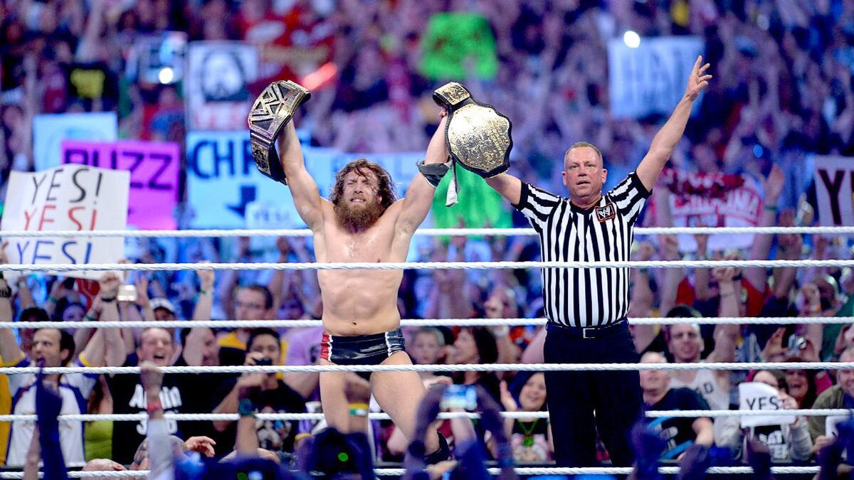 Daniel Bryan holding up two titles as referee Mike Chioda raises his arm at WWE WrestleMania 30