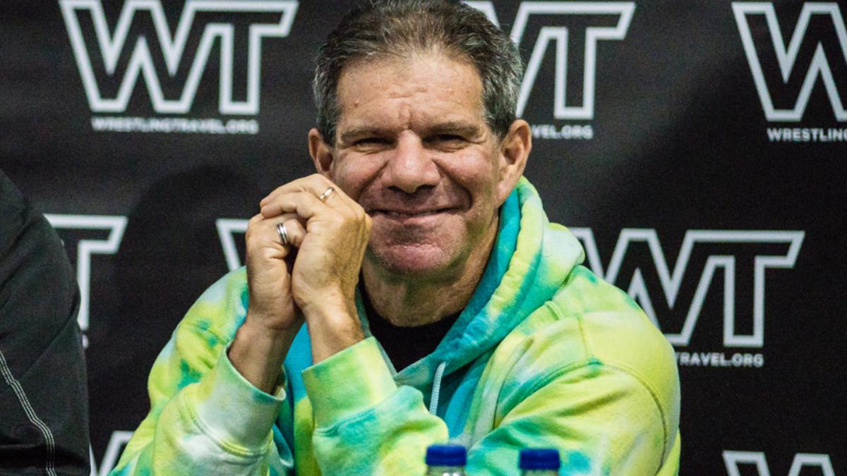 Dave Meltzer smiling on a panel, with his hands cupped in front of his face.