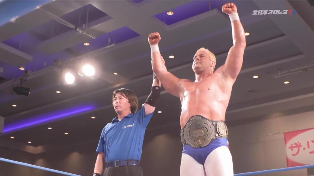 Davey Smith Jr. with raised fists in victory pose next to referee inside ring.