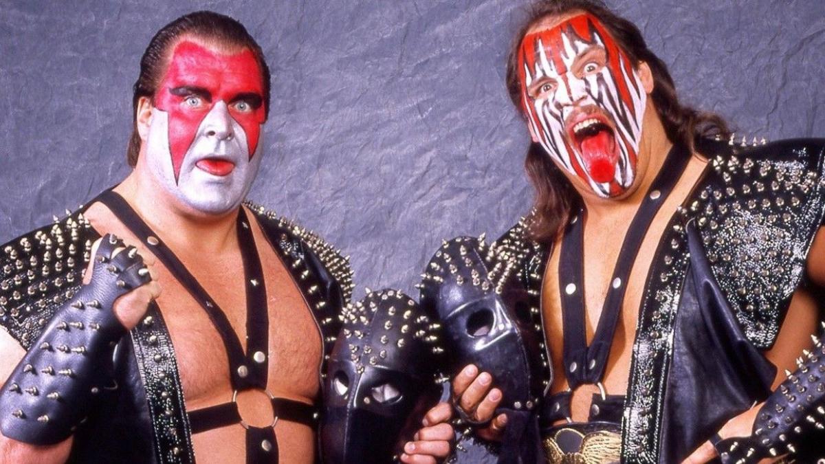 The team of Ax and Smash posing against a backdrop in their entrance gear, holding their masks.