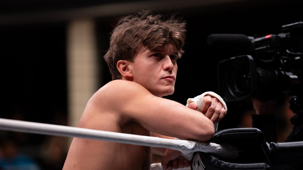 HOOK rests his arms on the top turnbuckle and stares at the crowd in the corner of a wrestling ring