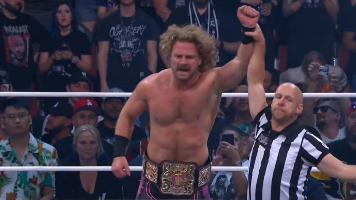 Hangman Page has his hand raised by the referee inside an AEW ring with a championship belt around his waist