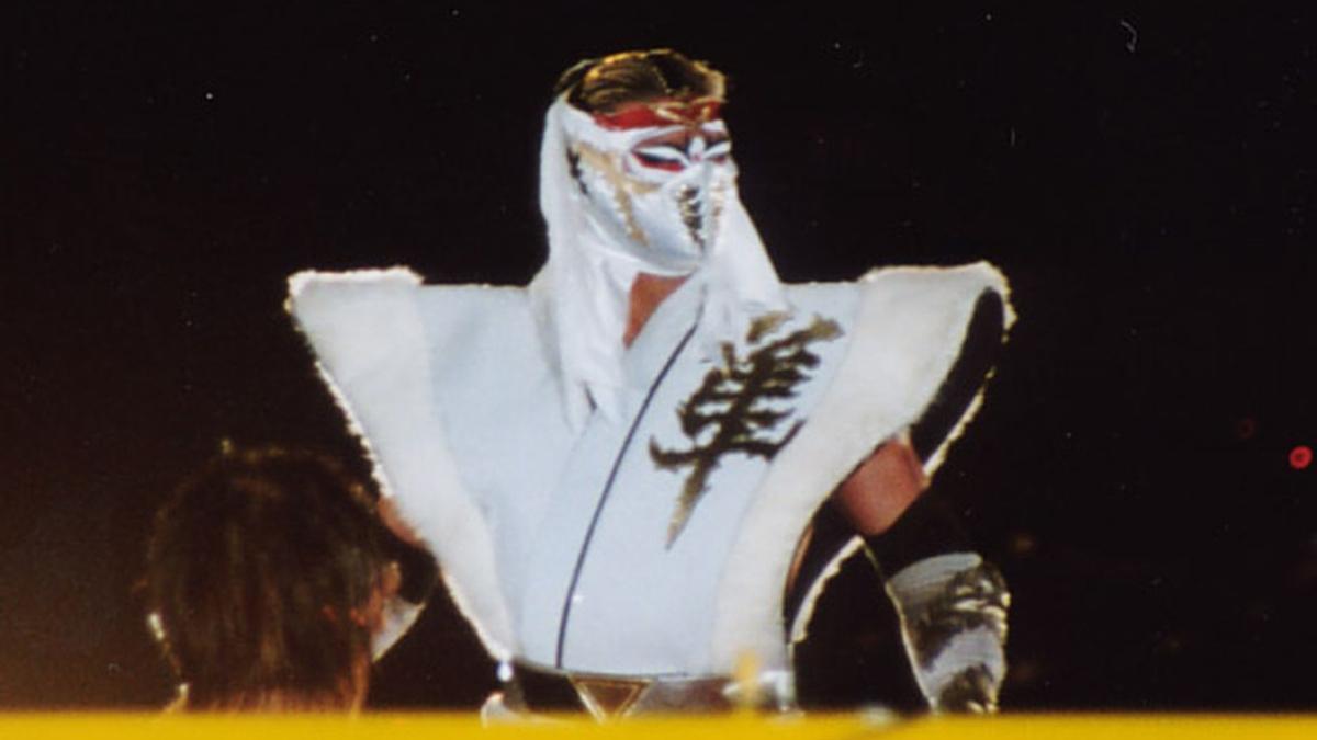 Hayabusa in white mask and sleeveless entrance jacket, looks at the crowd before a wrestling match