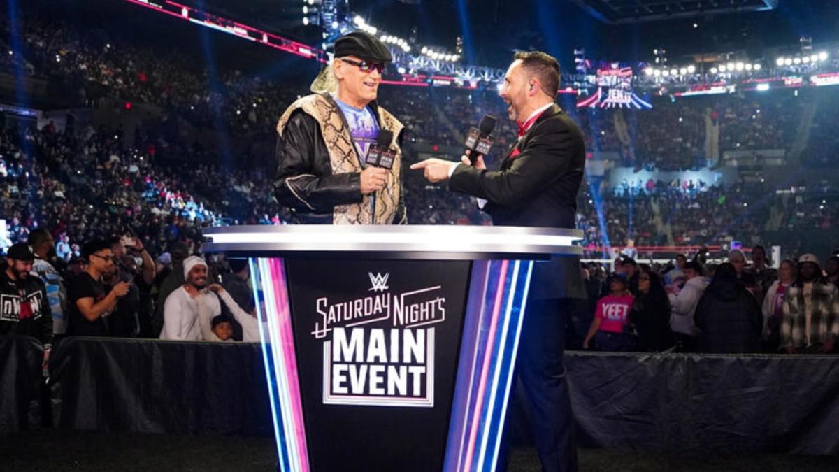 Jesse Ventura and Joe Tessitore talking by a Saturday Night's Main Event podium 