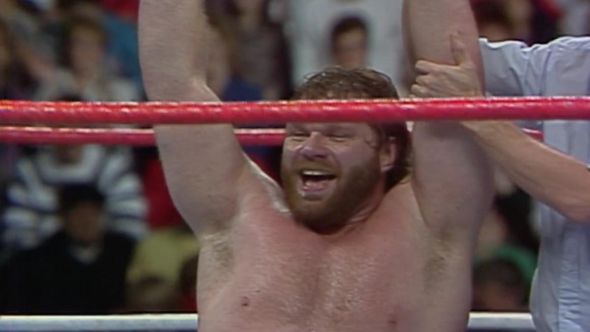 Hacksaw Jim Duggan on his knees with his arms up to celebrate the 1988 Royal Rumble win