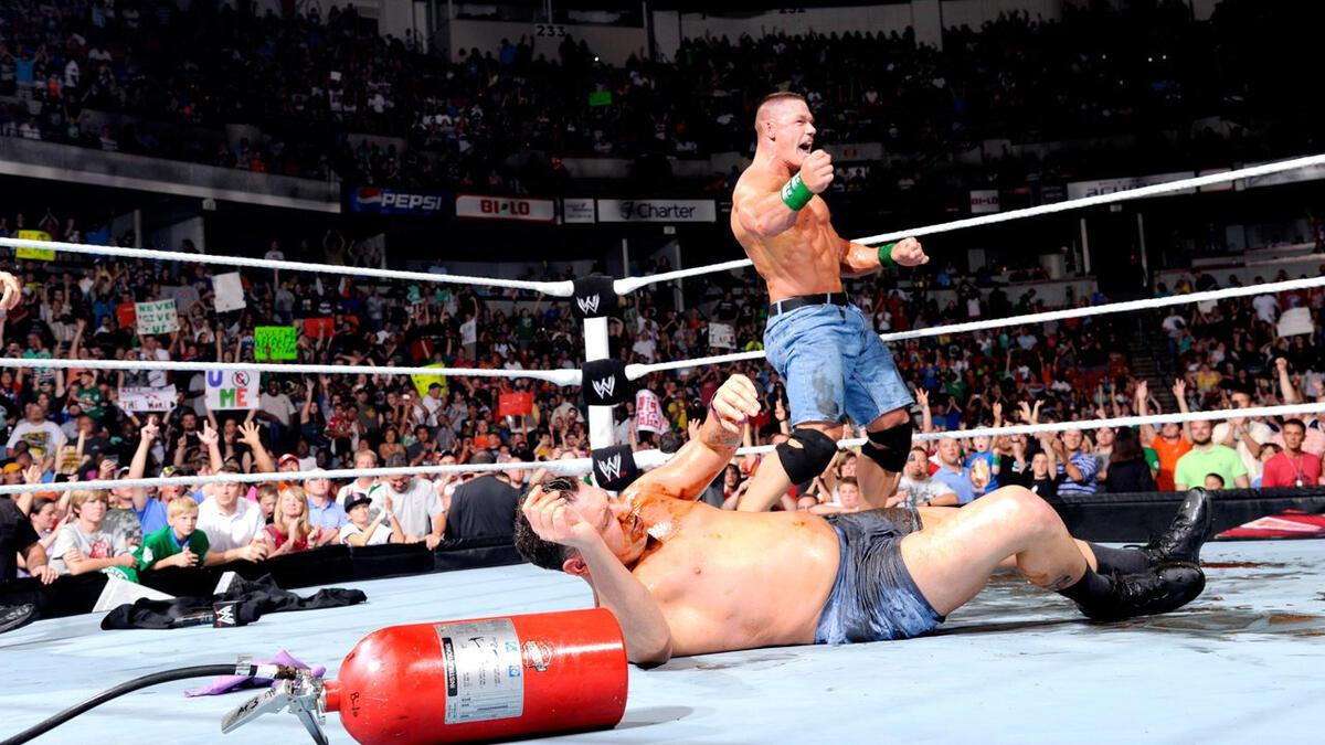 John Cena celebrates on June 6, 2012 episode of WWE Raw while Michael Cole lies down covered in BBQ sauce