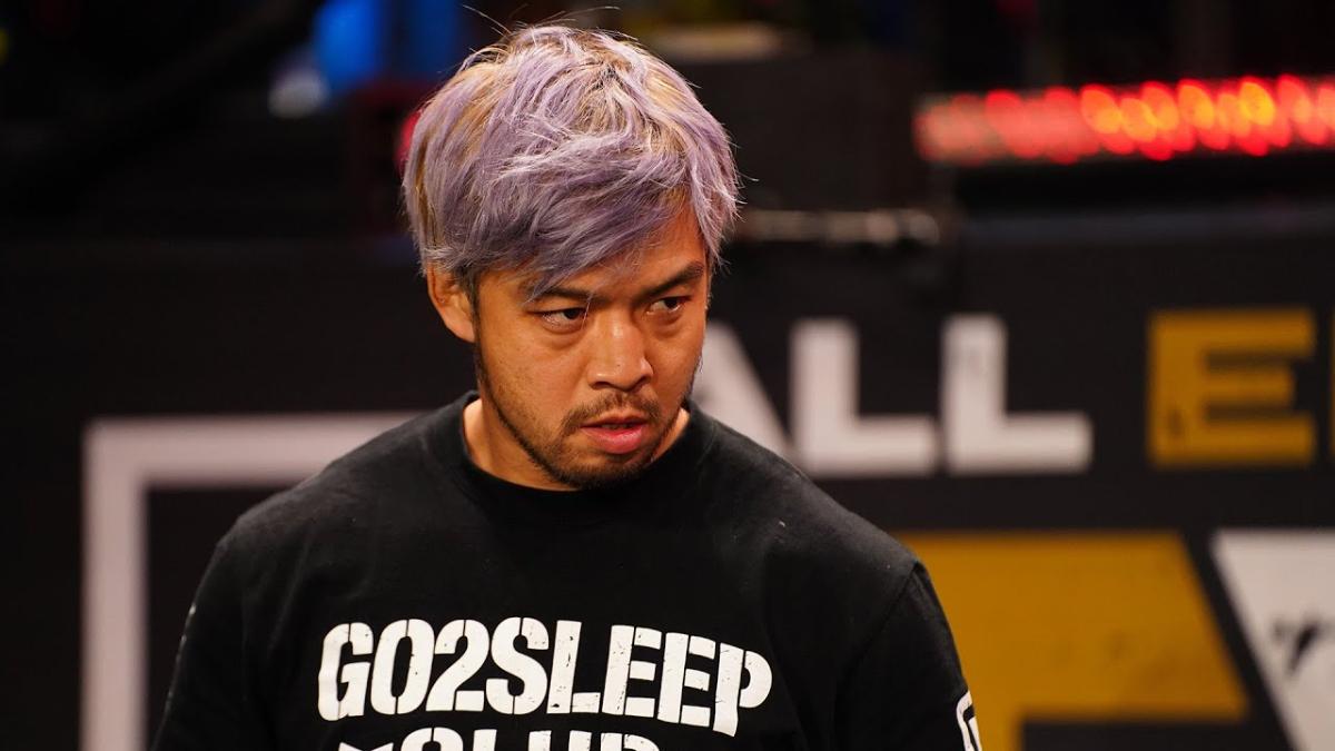 KENTA in a personalised Bullet Club t shirt frowning at someone off camera in a wrestling ring