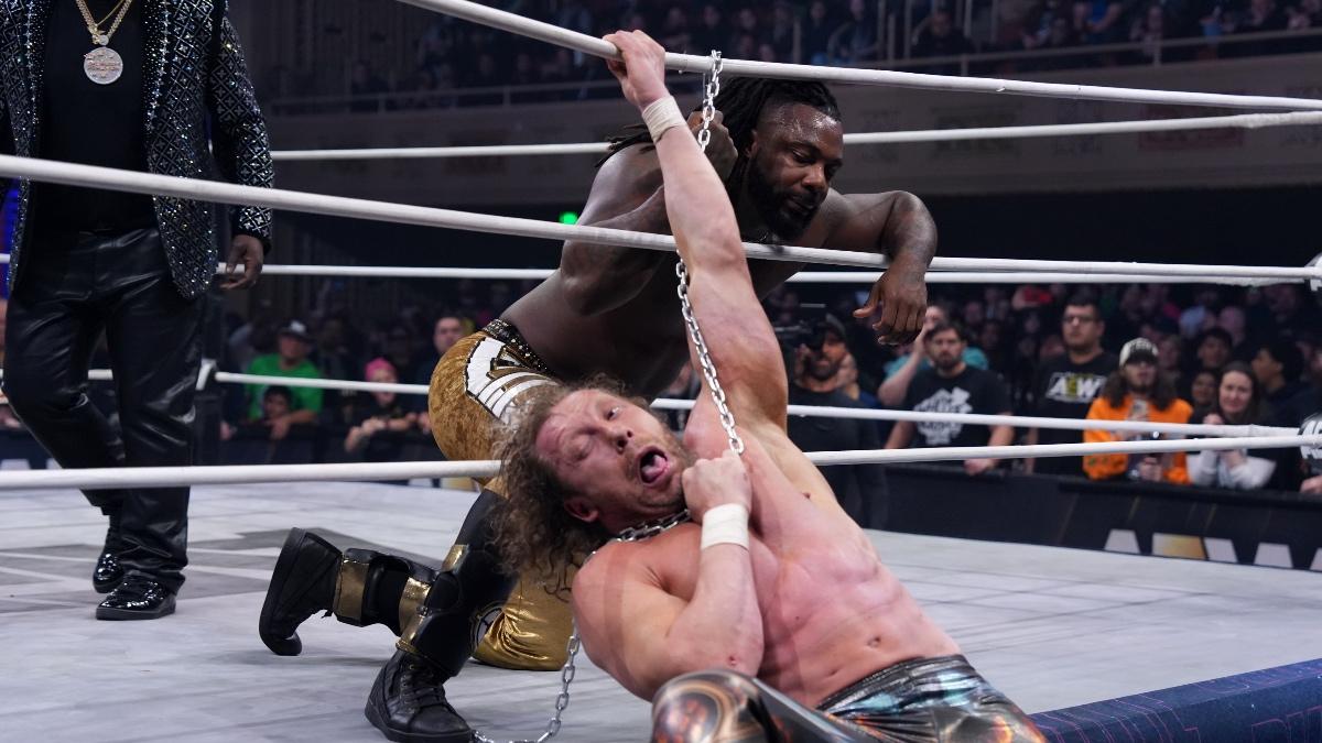 Swerve Strickland smirking while holding a chain that is storyline choking Kenny Omega