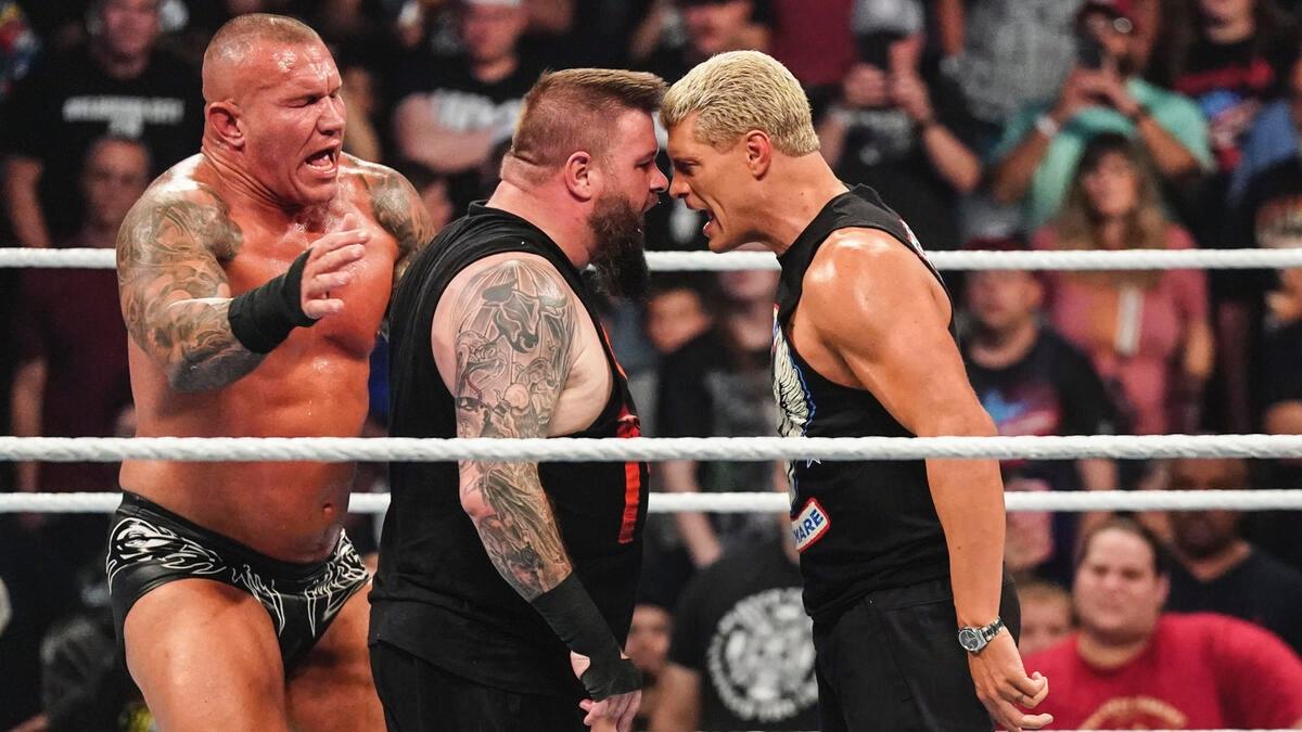 Kevin Owens and Cody Rhodes angrily looking at each other, touching foreheads as Randy Orton on the left hand side tries to separate them 