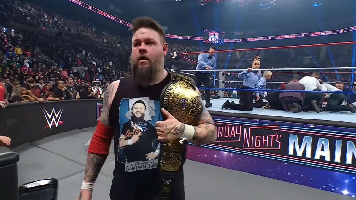 Kevin Owens wals away from a wrestling ring filed with referees with the WWE Winged Eagle Championship belt over his shoulder