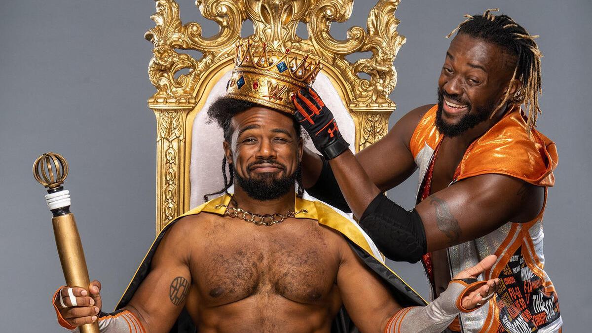 Xavier Woods wearing a crown and sitting on a throne as Kofi Kingston laughs next to him 