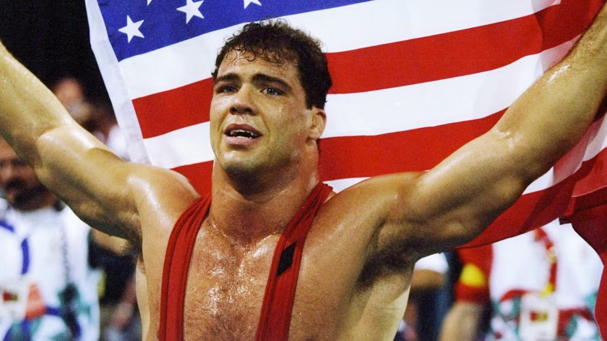 Kurt Angle in a singlet holding the American flag behind his head as he celebrates winning an Olympic gold medal