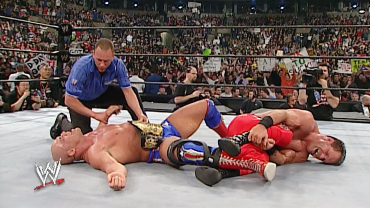 Kurt Angle lying down with the WWE Title lying across his chest as Chris Benoit lies next to him clutching his ankle