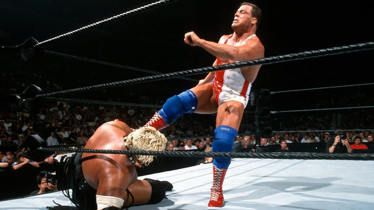 Kurt Angle kicking a downed Rikishi in a WWF wrestling ring.