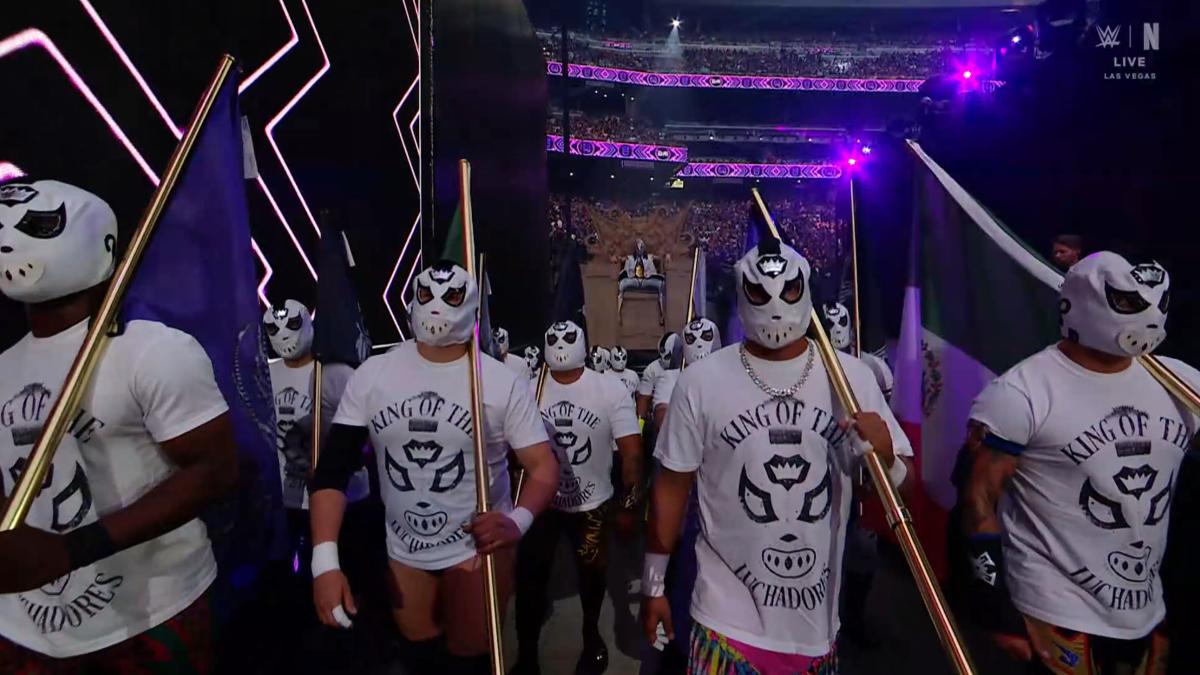 Dominik Mysterio sitting on a giant throne as a whole host of luchadores stand in front of him 