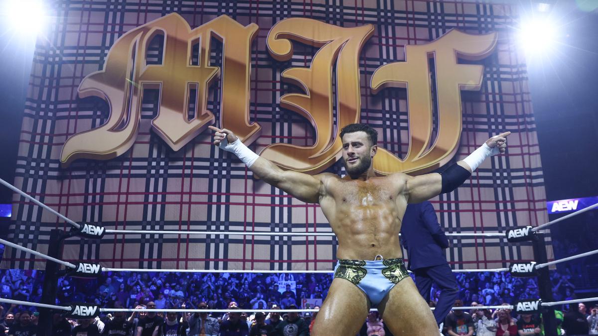 MJF kneeling in the ring with a giant 'MJF' flag behind him