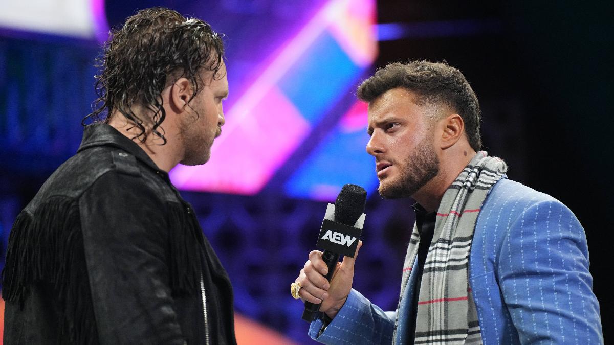 Hangman Adam Page in a leather jacket stares at MJF who is in a suit and speaking into an AEW microphone