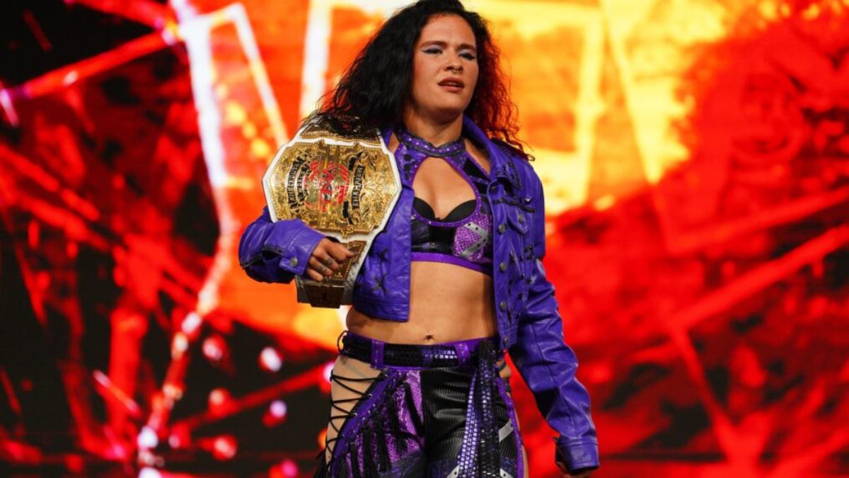 Masha Slamovich walks to a wrestling match with a championship title belt on her shoulder