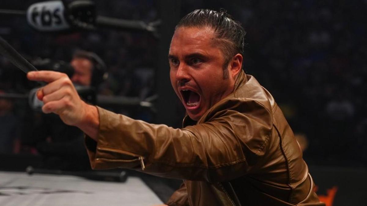 Matt Menard in a brown leather jacket angril points at a wrestling ring from the outside