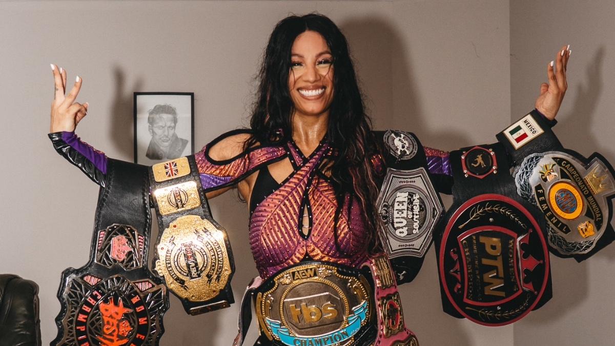 Mercedes Moné with her arms outstretched while covered in pro wrestling belts 