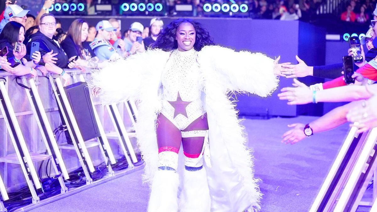 Naomi wearing all-white gear with her arms outstretched while walking to the ring at WWE Elimination Chamber