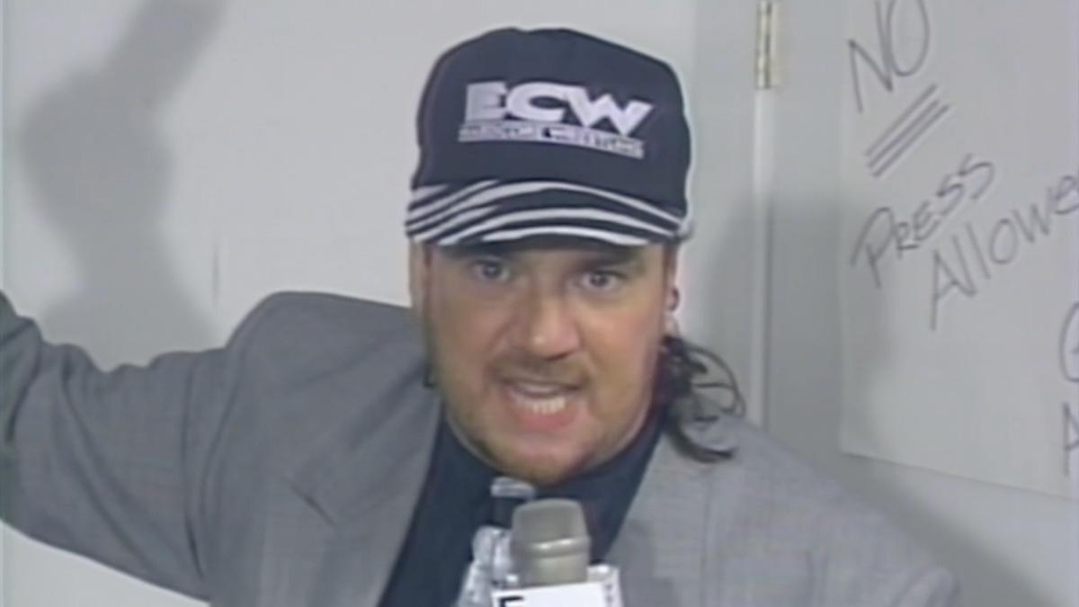 Paul Heyman wearing a grey suit and ECW hat