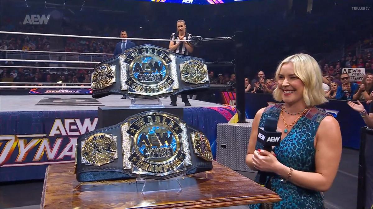 Renee Paquette looks at  a set of AEW championship belts in front of a wrestling ring