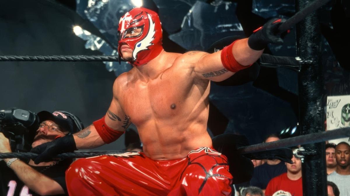 Rey Mysterio wearing red leather pants and a red mask kneeling in the corner of a pro wrestling ring