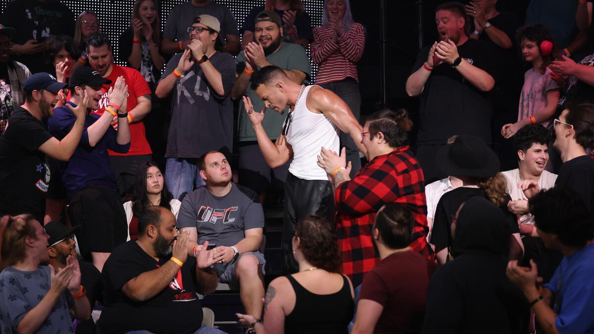 Ricky Starks in a white vest doing his signatur hand-to-face pose in the crowd at a wrestling event.